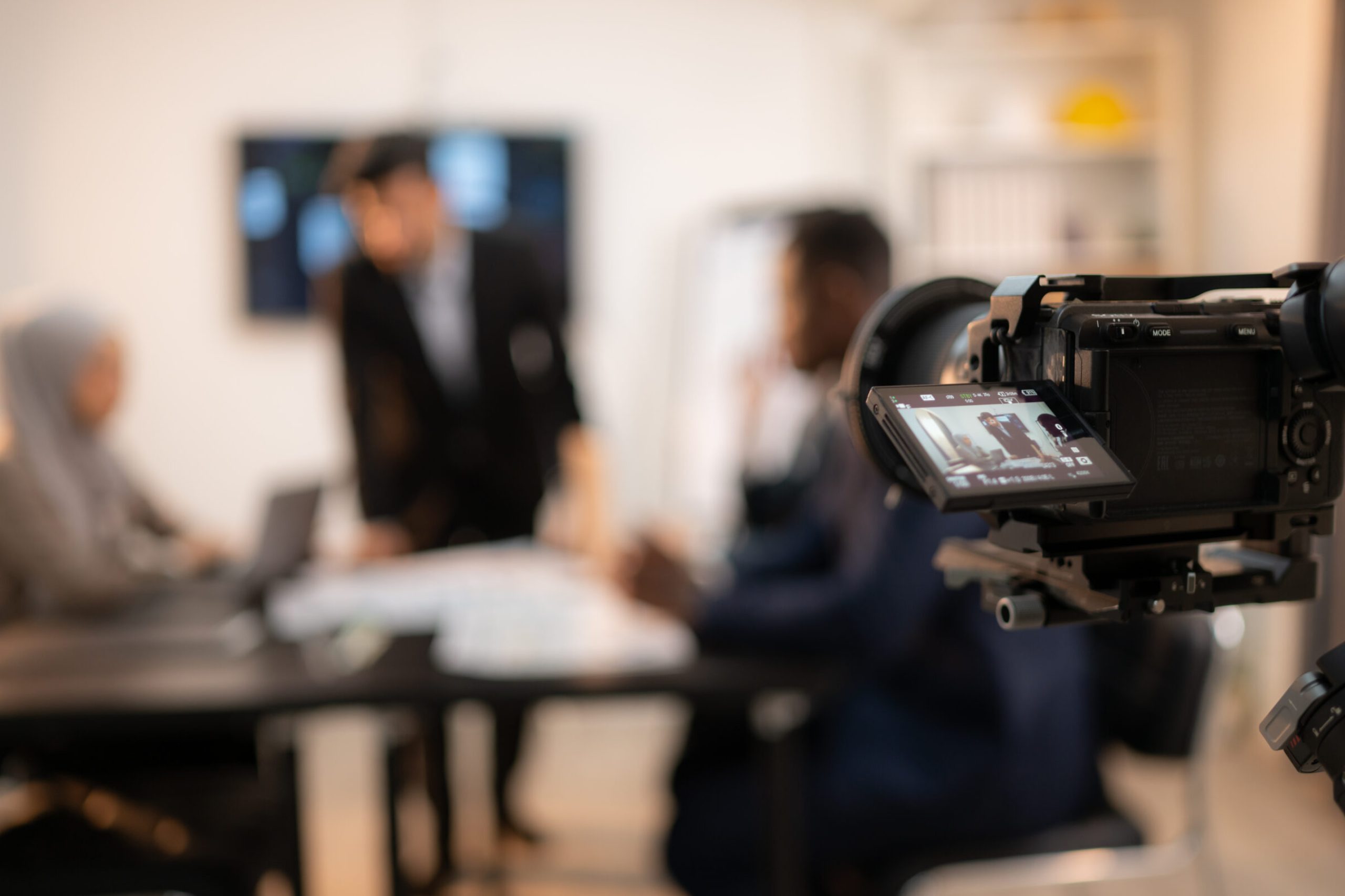 Blurred image of video camera on tripod and blurred business people working in background, Concept of shooting video company profile